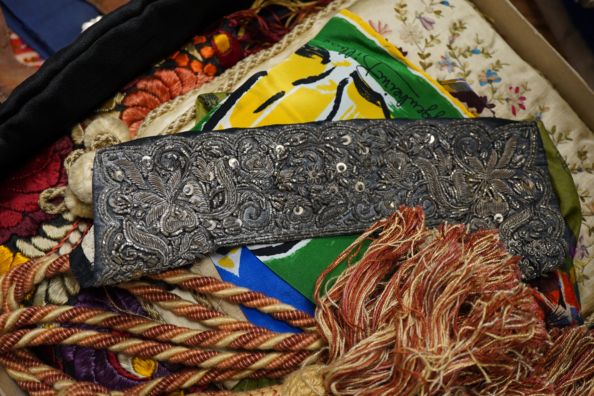 A collection of textiles: a ribbon work hankie and pyjama case, a metalwork collar, a coloured printed shawl, a nurses belt and embroidered belt, an advertising Guggenheim Bilbau hankie etc (10). Hankie case 22cm square.